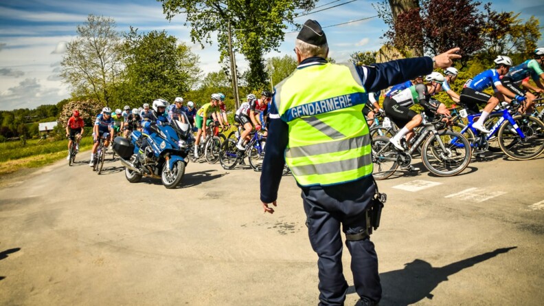 Gendarme équipé d'un chasuble jaune gendarmerie, de dos, indiquant le sens de la course aux cyclistes